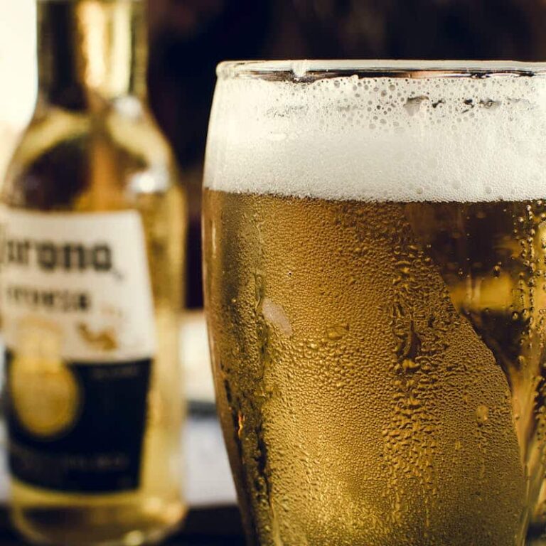 a glass of beer with a bottle of corona at the background