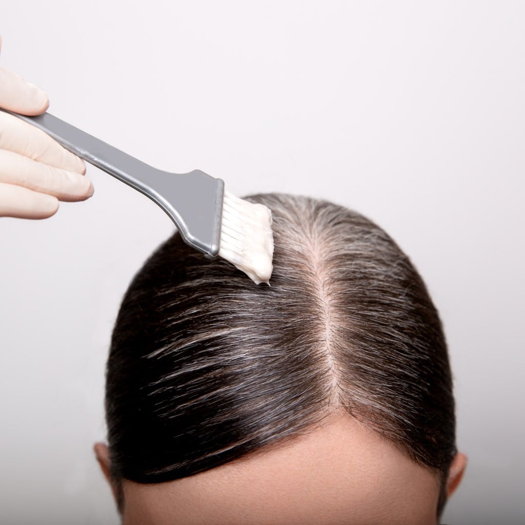 Woman dyeing grey hair root with brush and hair color