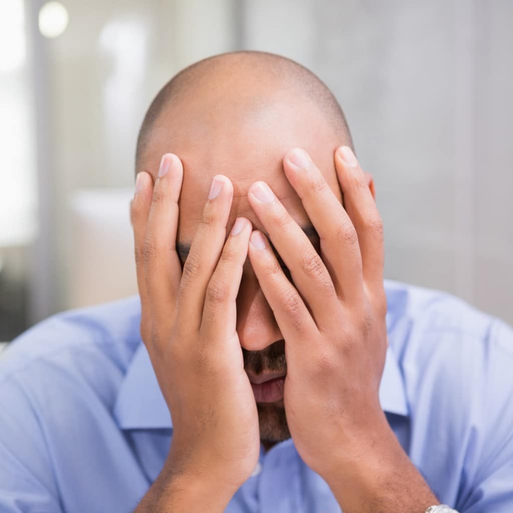 a bald man with both his hands on his face