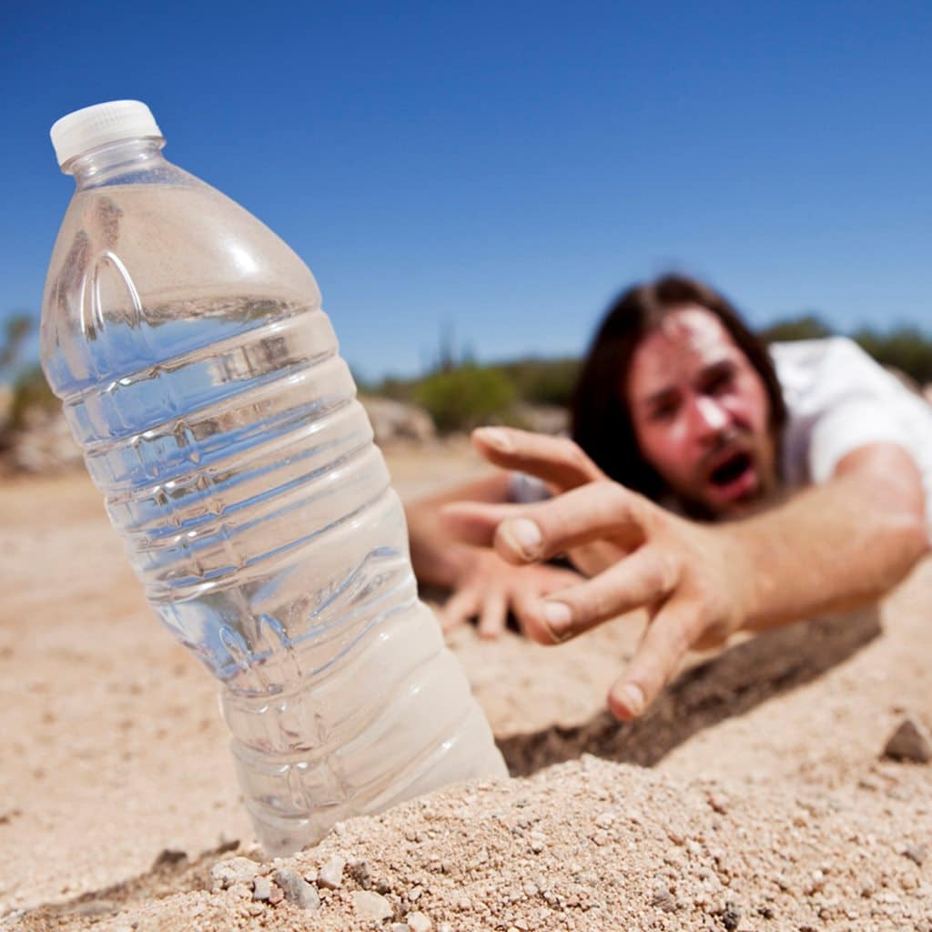 Dehydrated man crawling through the desert reaching for bottle of water