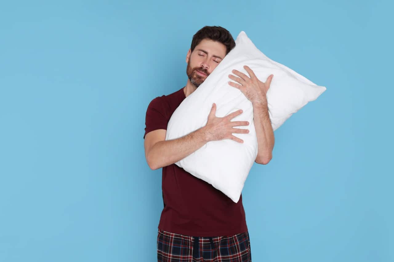 sleepy man hugging soft pillow on light blue background